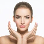 Beautiful face of young caucasian woman with perfect health skin  - isolated on white.  Skin care concept. Female Model touches face.